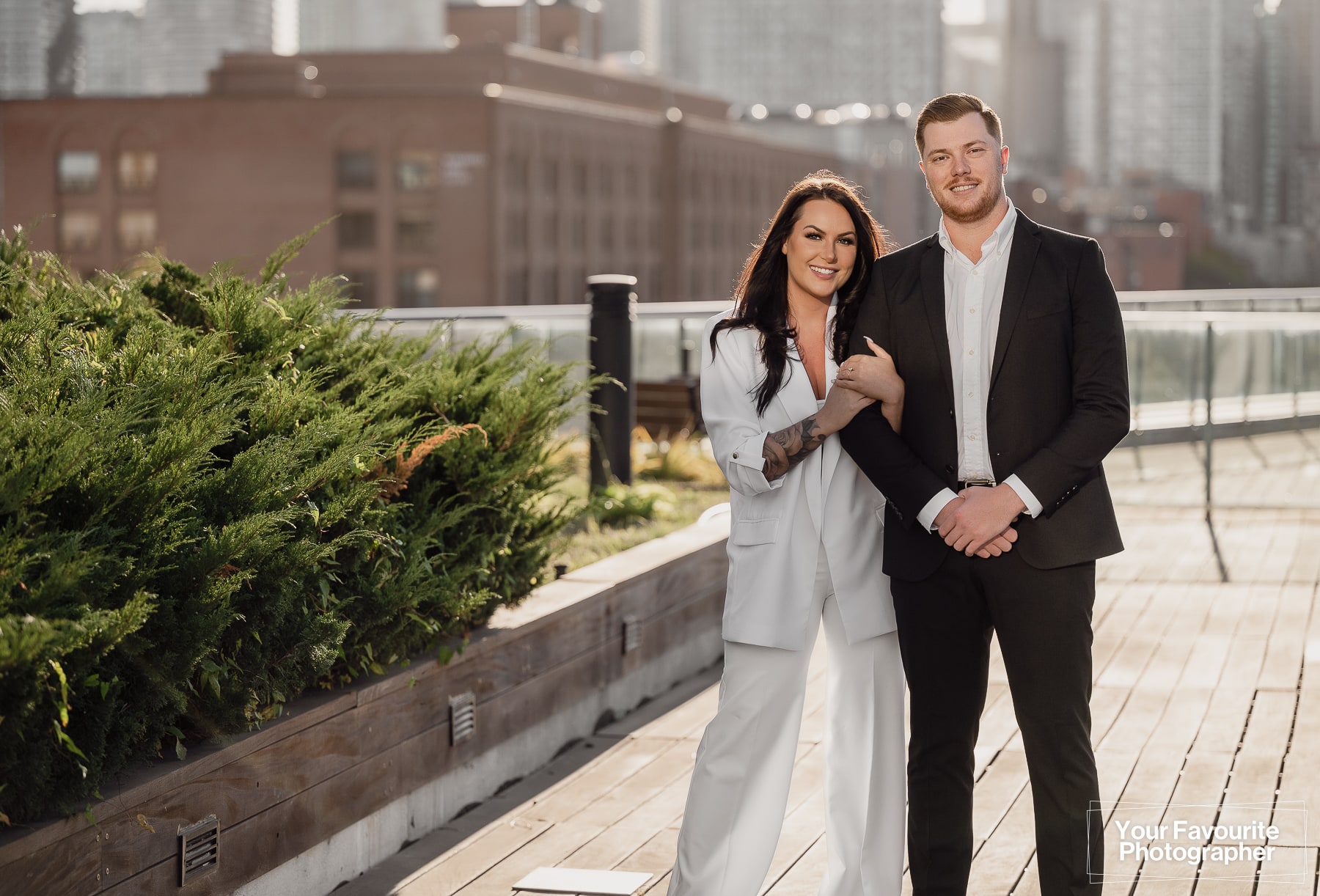 Engaged couple Sam and Rob stand on a Distillery District rooftop patio overlooking the Toronto skyline for their engagement photo shoot