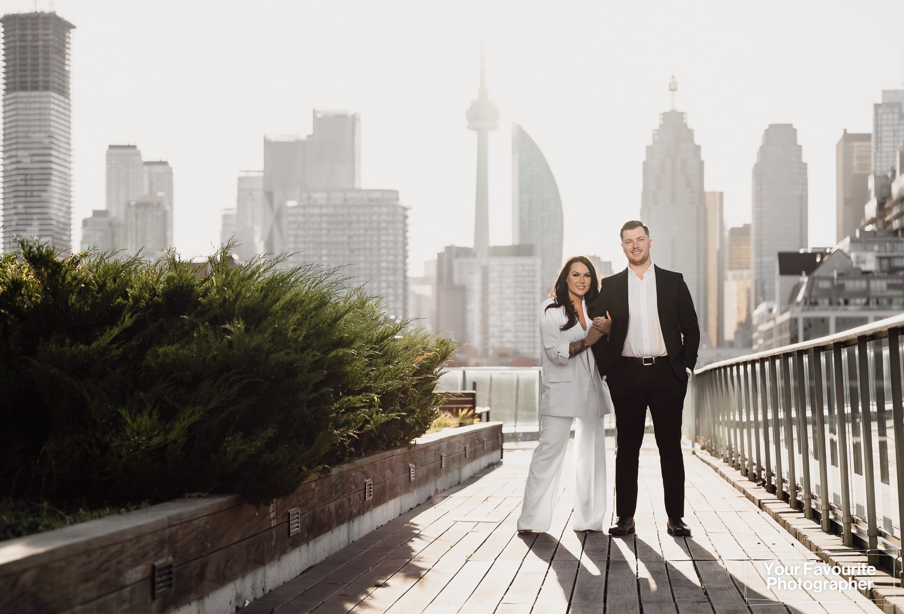 Engaged couple Sam and Rob stand on a Distillery District rooftop patio overlooking the Toronto skyline for their engagement photo shoot
