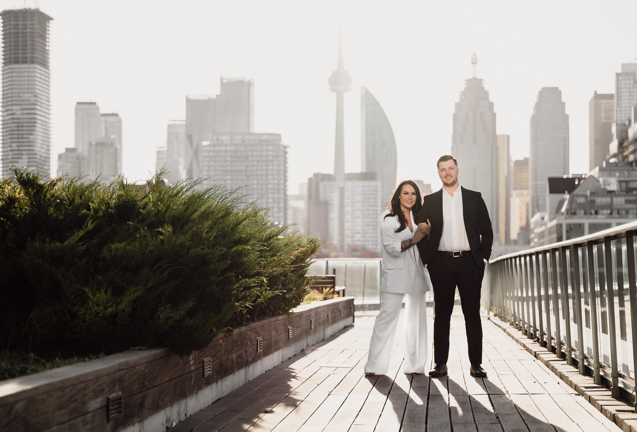 Engaged couple Sam and Rob stand on a rooftop patio overlooking the Toronto skyline for their engagement photo shoot
