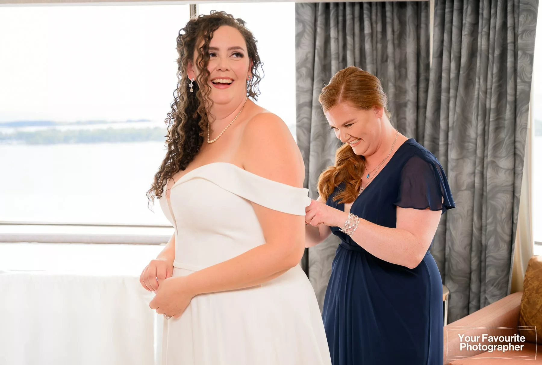 Bridesmaid helping bride fasten her wedding dress
