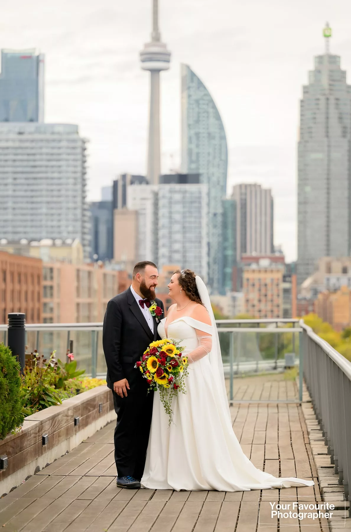Newly married couple Emily and Niko pose on a rooftop patio with the skyline of downtown Toronto visible in the background