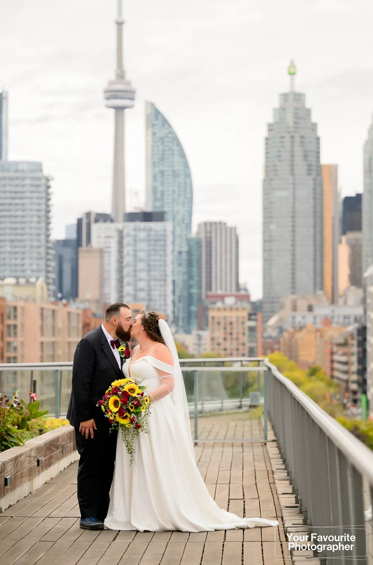 Newly married couple Emily and Niko kiss on a rooftop patio with the skyline of downtown Toronto visible in the background