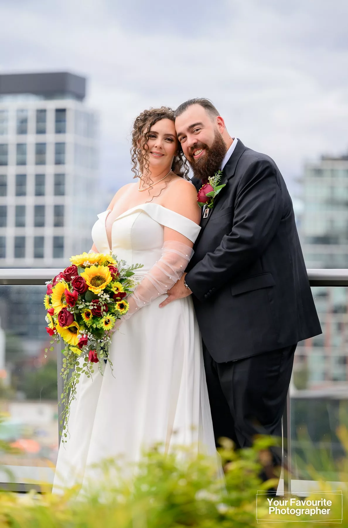 Bride and groom pose on a rooftop patio with a cityscape in the background and a garden in the foreground