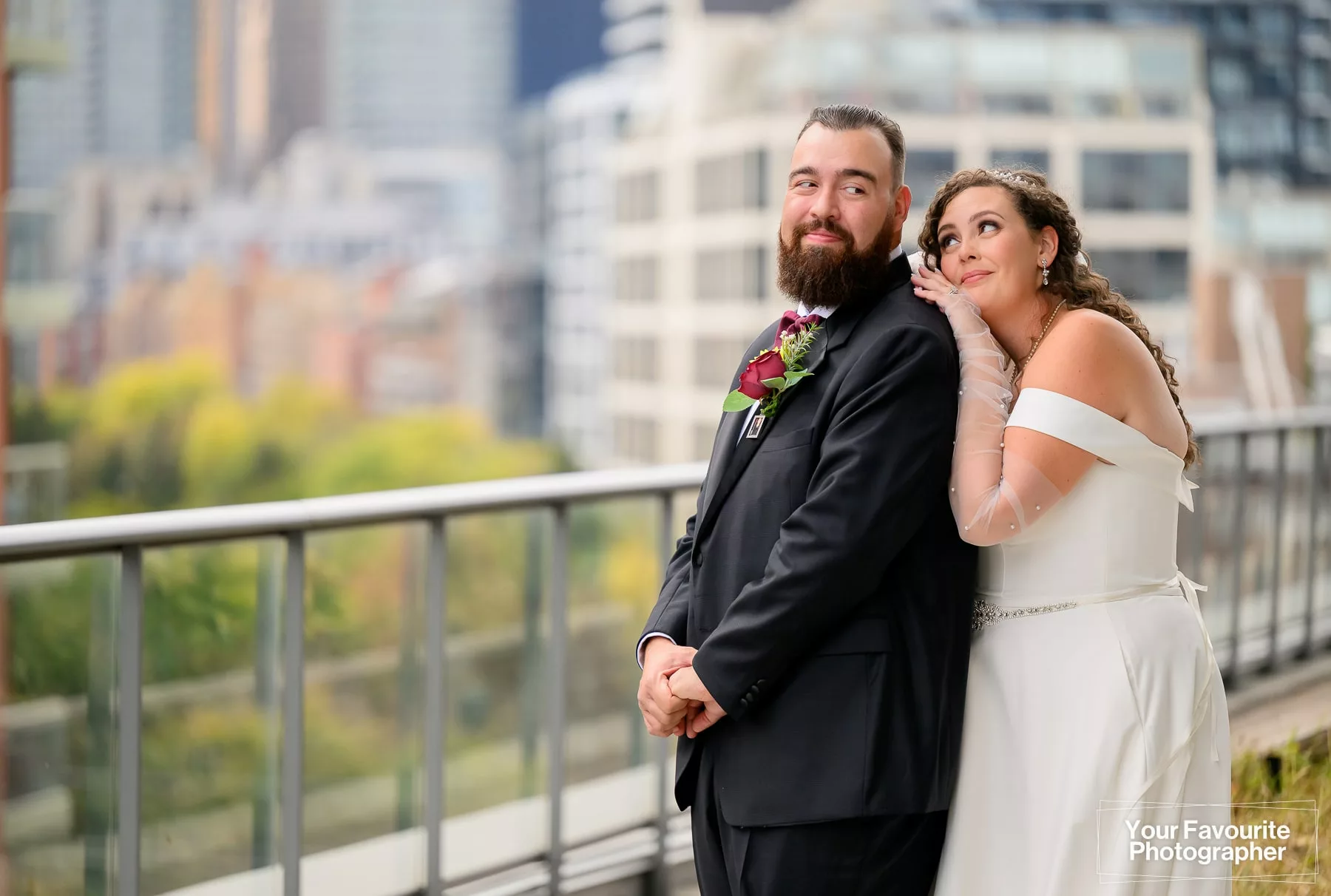 Bride leans against a groom as they pose on a rooftop patio with a garden and city in the background