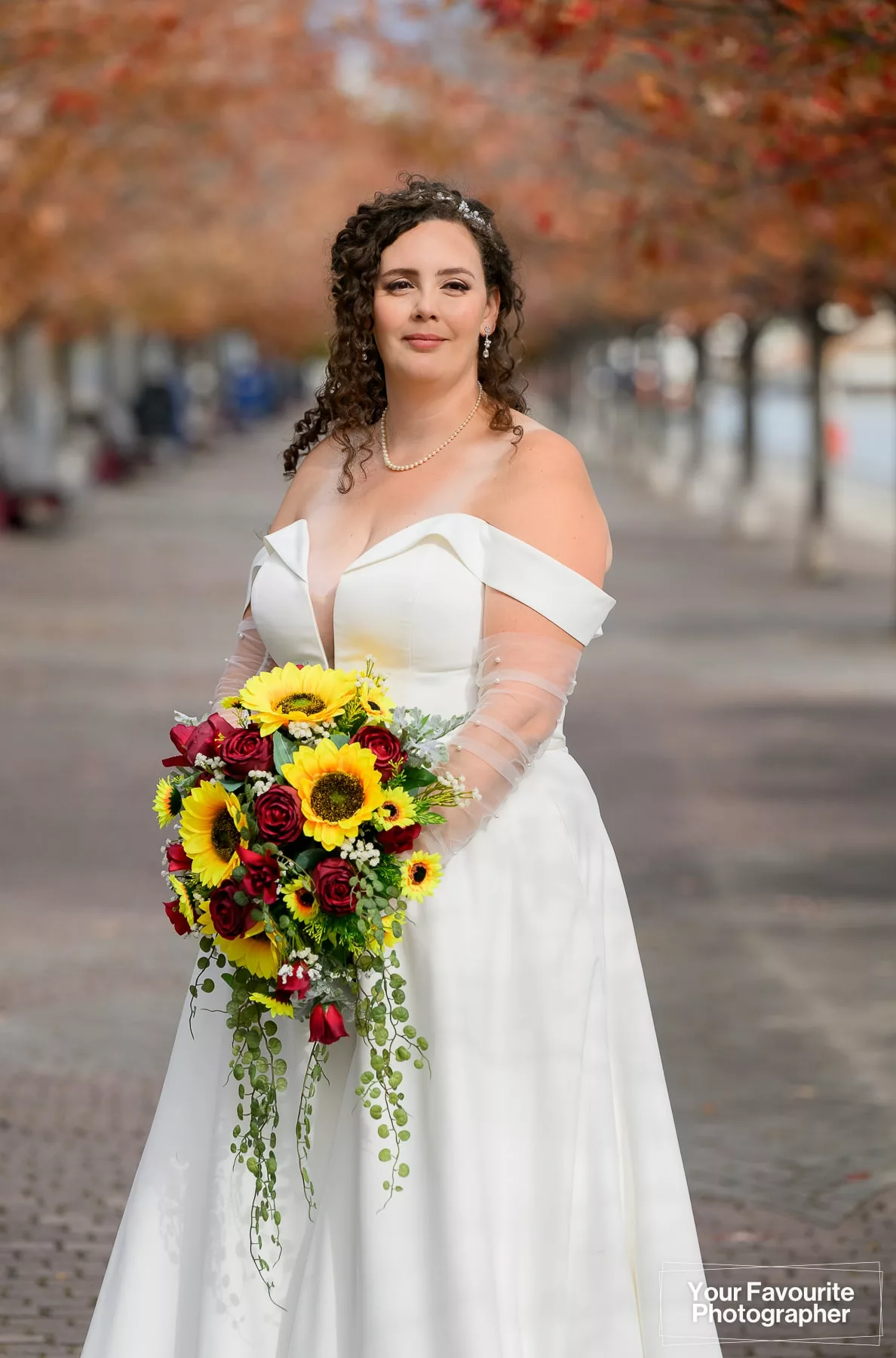 Bride with bouquet poses on the Water's Edge Promenade in downtown Toronto, with fall foliage in the background
