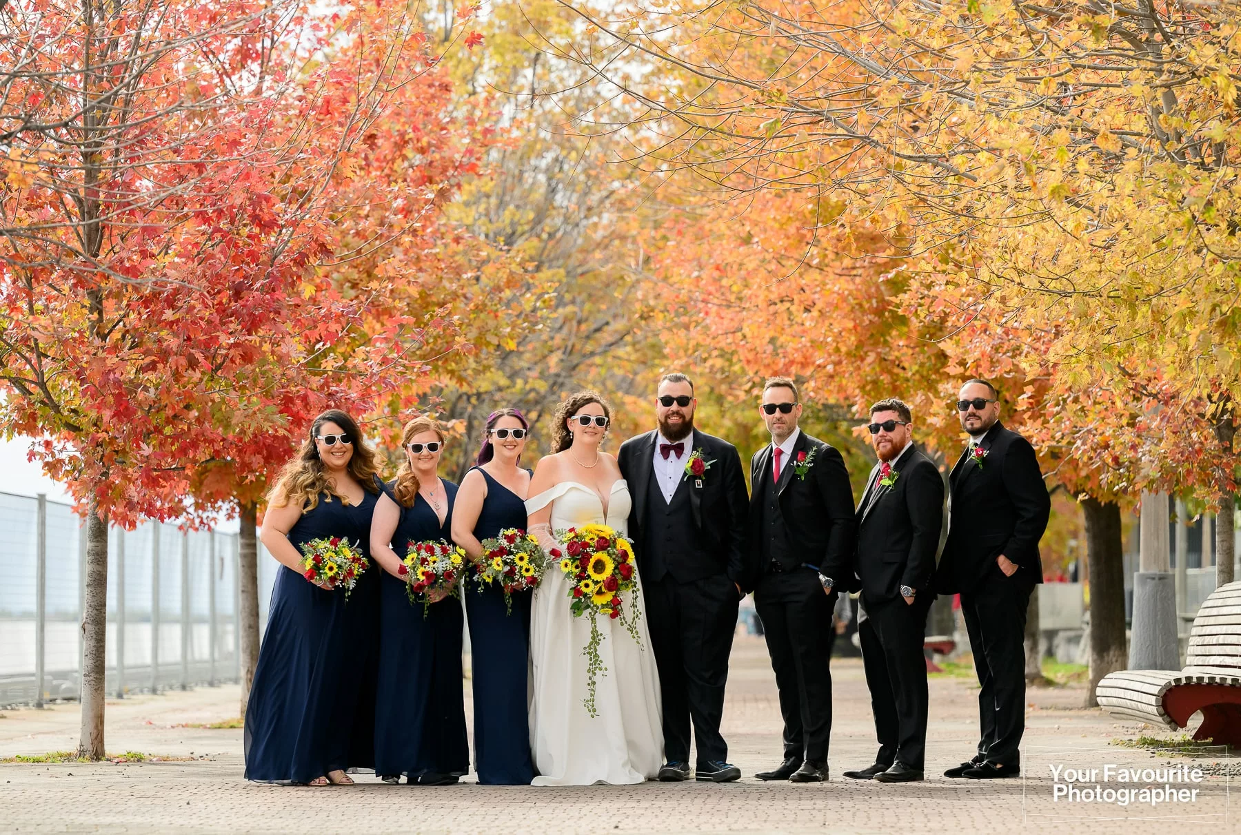 Wedding party in sunglasses poses on the Water's Edge Promenade in downtown Toronto, surrounded by fall foliage