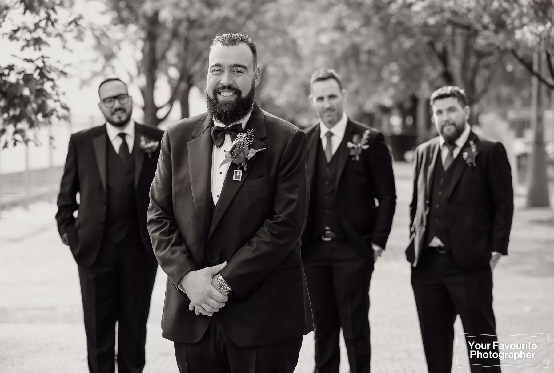 Black and white photo of a groom with his groomsmen in the background