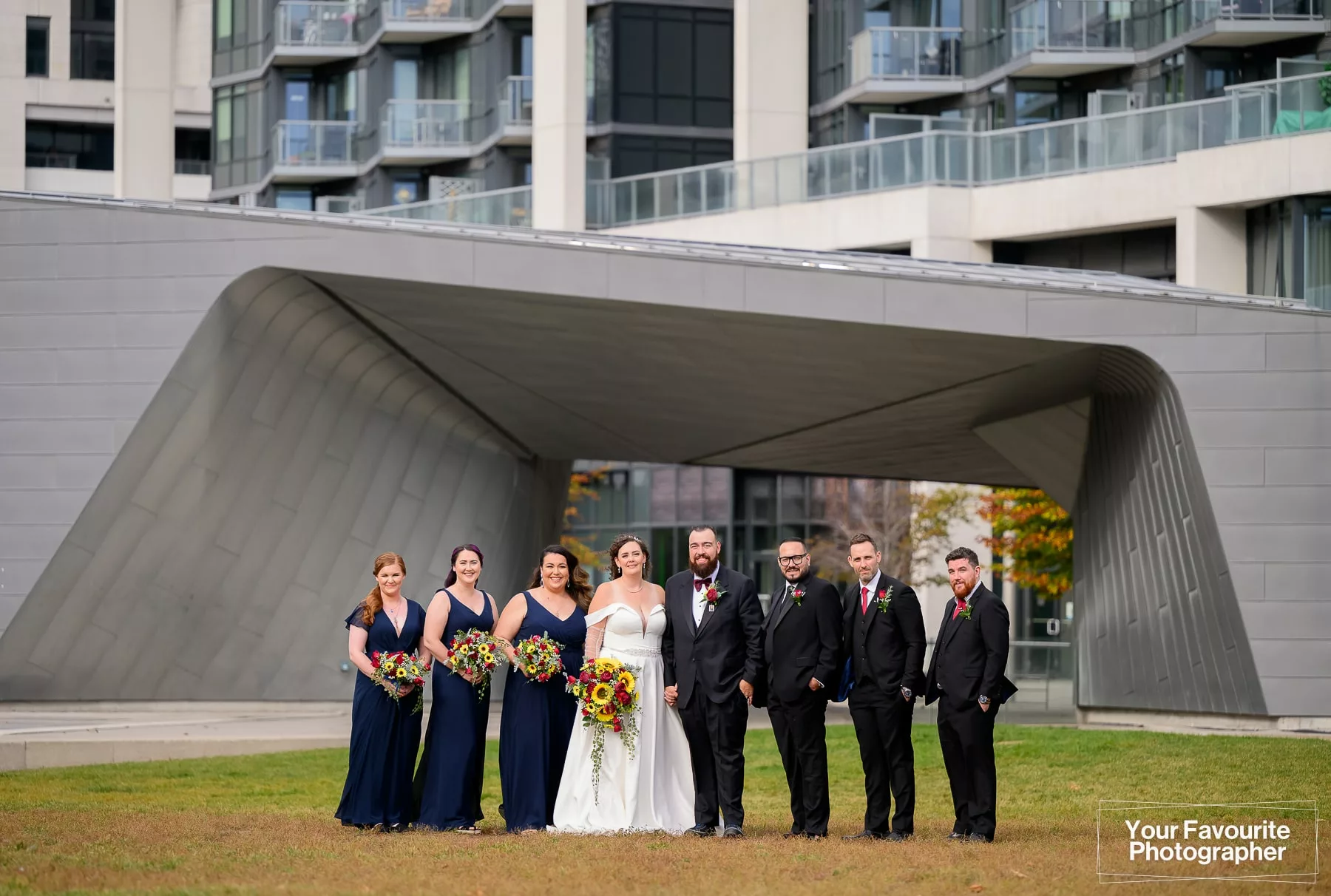 Wide view of a wedding party standing in front of the pavilion at Sherbourne Common in downtown Toronto