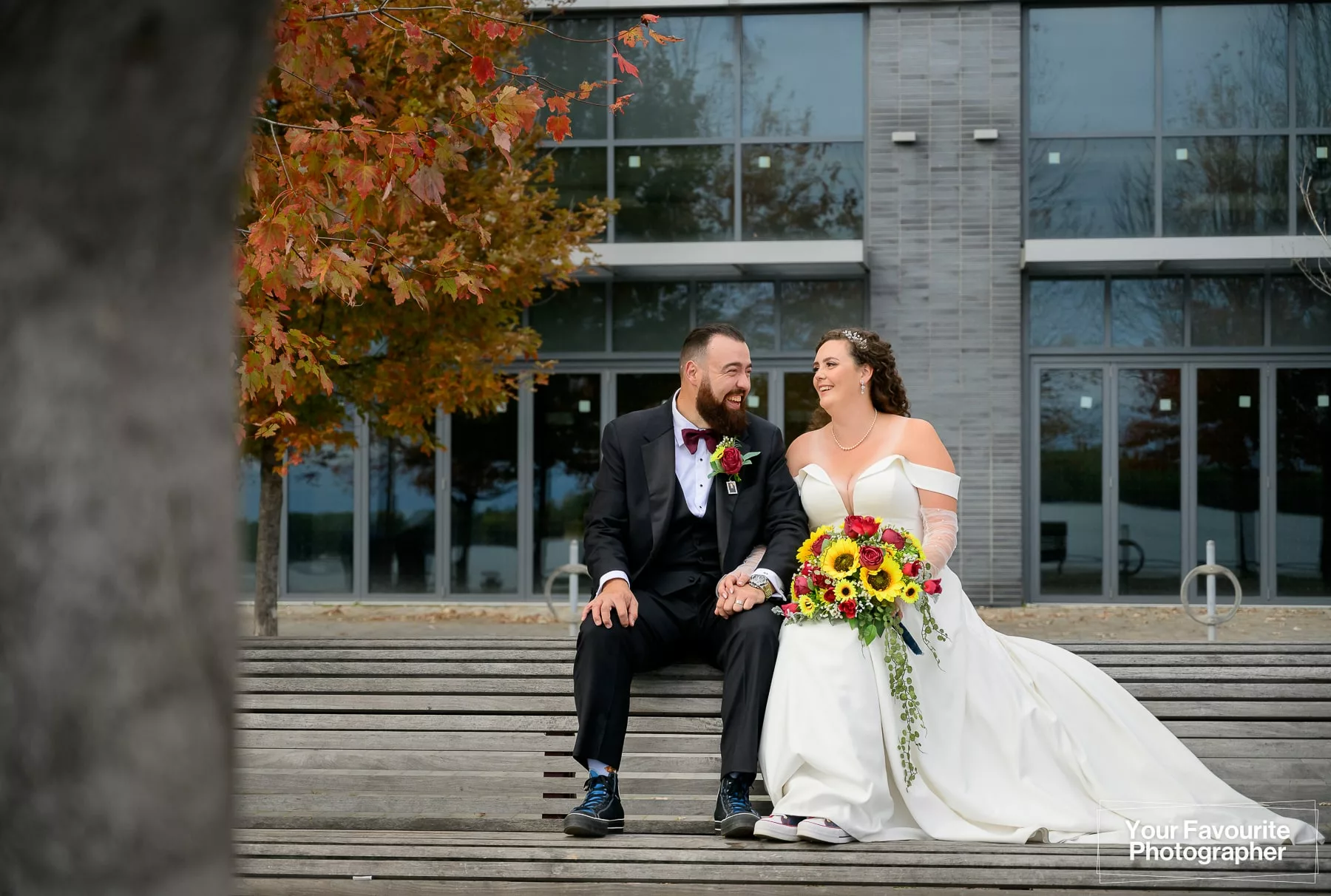 Bride and groom sit on a bench in downtown Toronto, near Sherbourne Common, on the Water's Edge Promenade