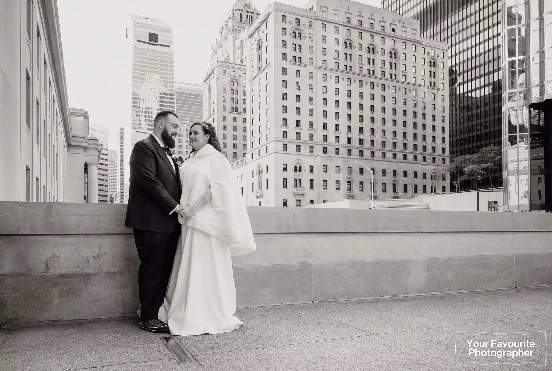 Black and white photo of a bride and groom posing in front of Union Station on Front St in downtown Toronto, with the Royal York hotel in the background