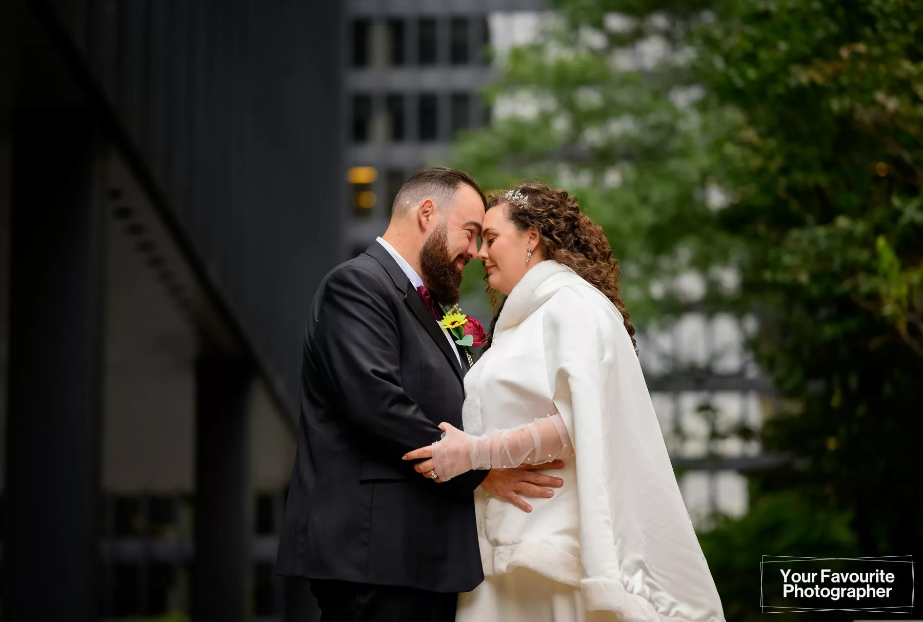 Bride and groom pose for a formal portrait with their foreheads together, in front of downtown Toronto office buildings, on Pearl St