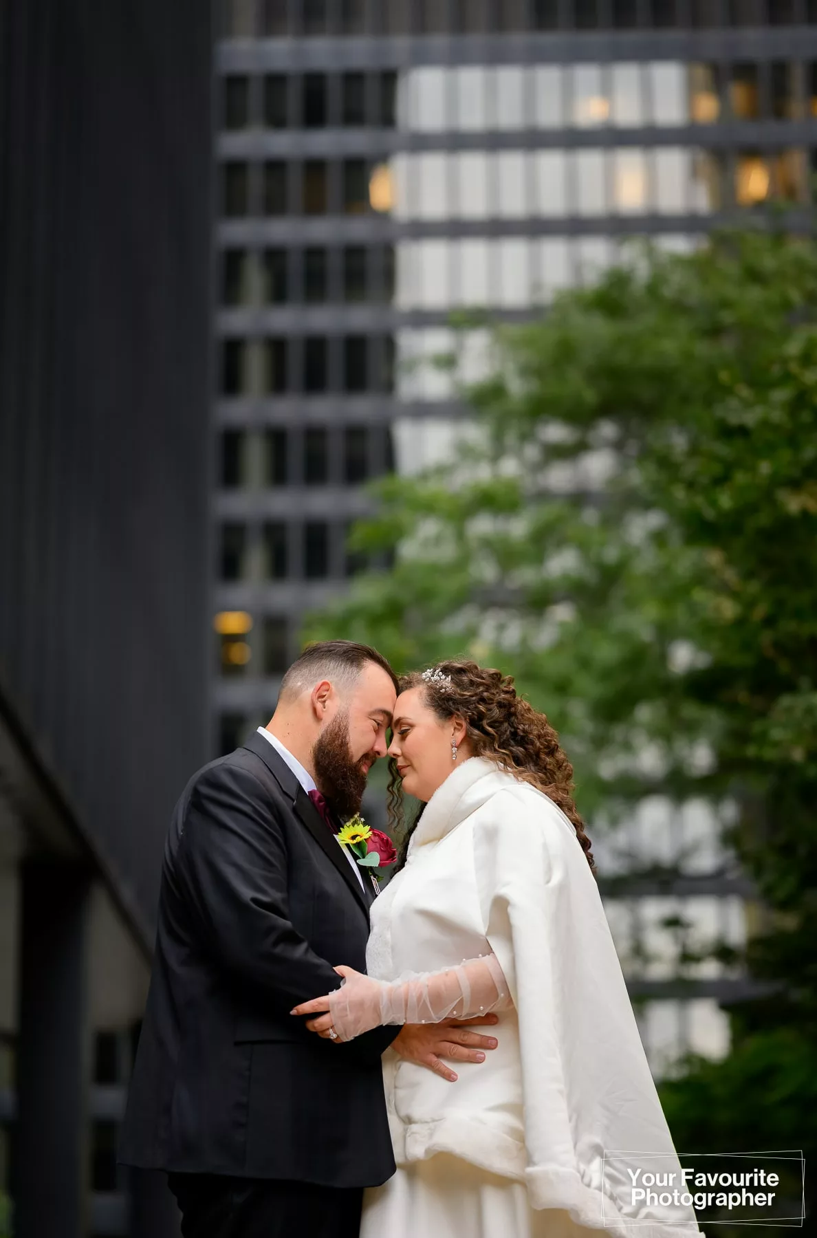Bride and groom pose for a formal portrait with their foreheads together, in front of downtown Toronto office buildings, on Pearl St