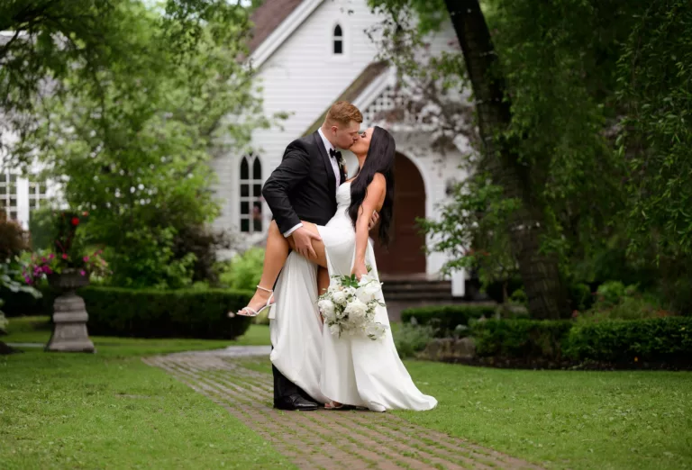 Groom Robert dips bride Samantha in front of a chapel