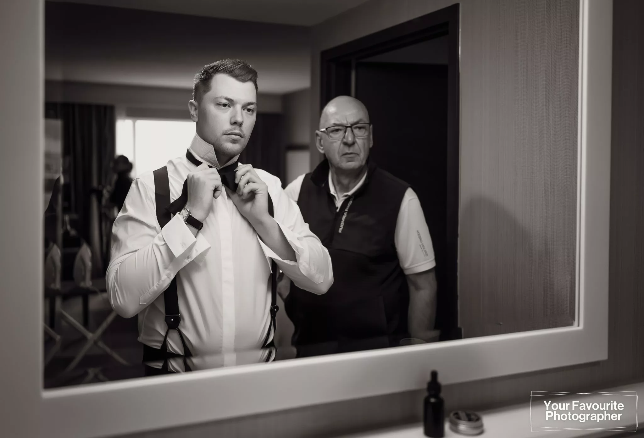 Groom looks in the mirror to put on his bowtie on the morning of his wedding