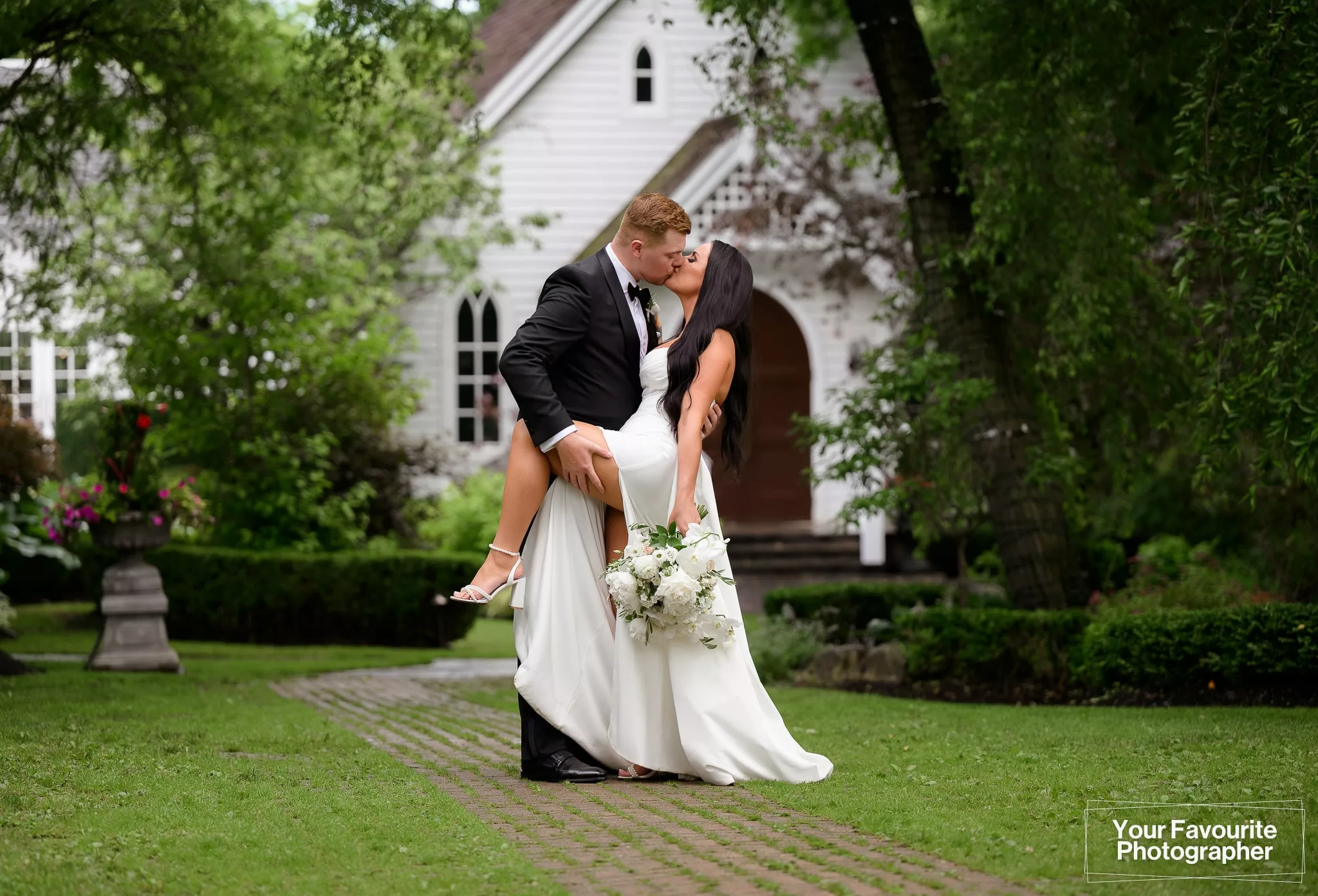 Samantha and Robert posing outside the chapel at The Doctor's House on their wedding day, sharing a kiss with a dip