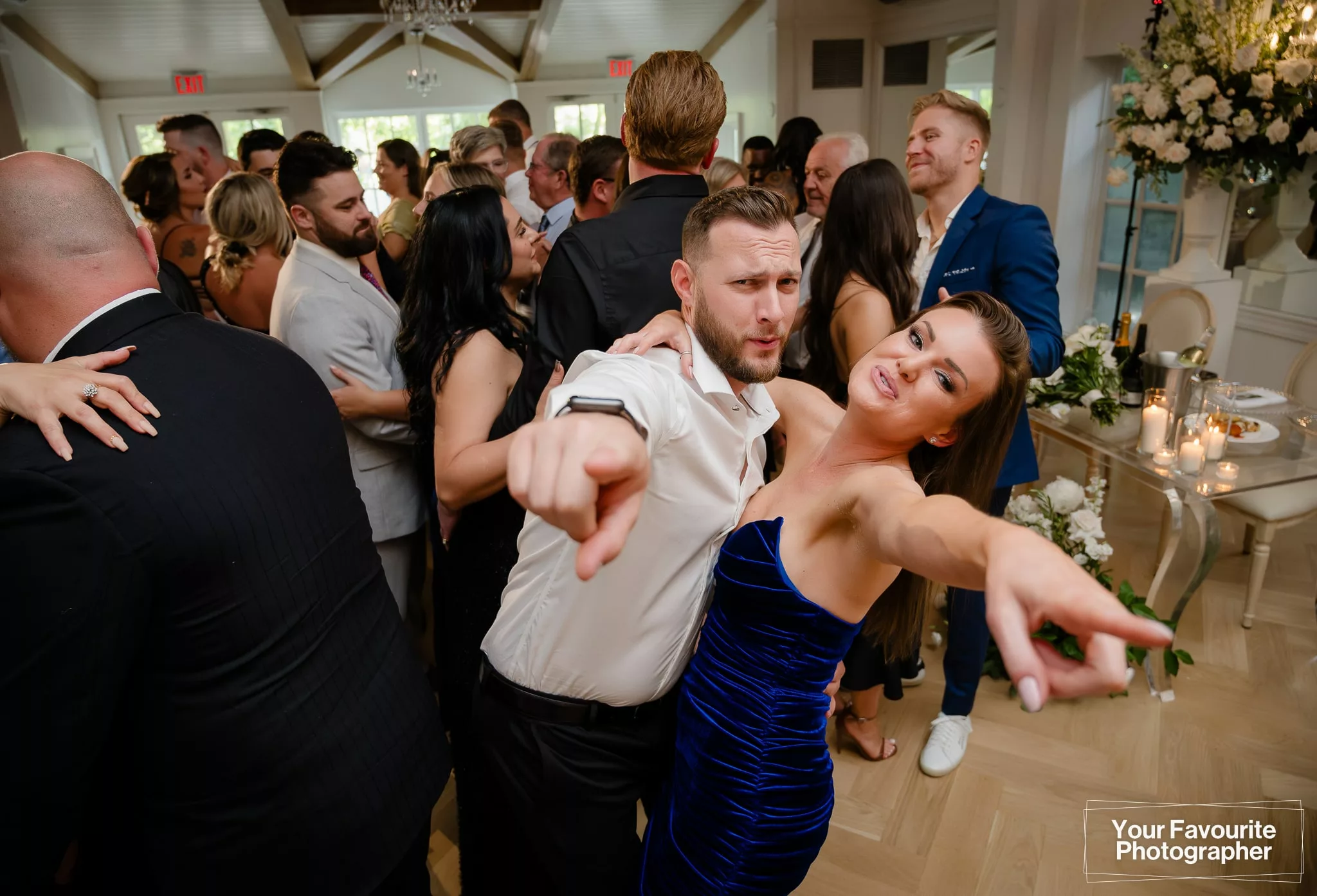 Wedding guests point at the camera while on the dance floor